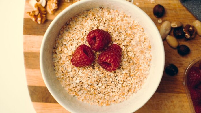 Cholesterin senken Cholesterin senken: Schale mit Haferflocken und Himbeeren, daneben Nüsse auf einem Holzbrett