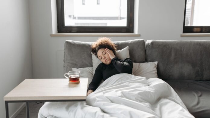 Grippe oder Erkältung Grippe oder Erkältung: Frau liegt krank unter einer Decke auf dem Sofa, daneben eine Tasse Tee
