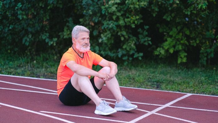 Regeneration nach dem Marathon Regeneration nach dem Marathon: älterer Läufer sitzt erschöpft auf der Laufbahn