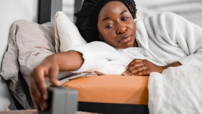 Zeitumstellung 2026 Zeitumstellung 2026: Frau im Bett greift morgens nach dem Wecker